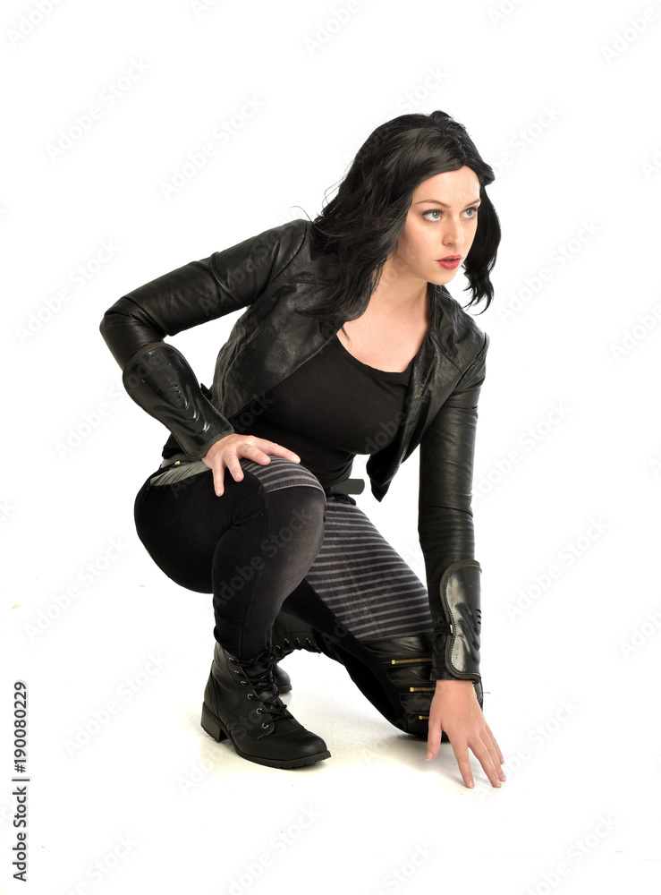 full length portrait of black haired girl wearing leather outfit. sitting pose, isolated on a white studio background. full length portrait of black haired girl wearing leather outfit. sitting pose, isolated on a white studio background.