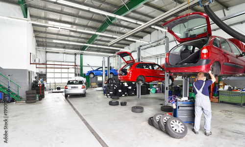 Reifenwechsel und Reparatur von Autos in einer Werkstatt - Aussstattung und Mechaniker arbeitet am Fahrzeug auf einer Hebebühne