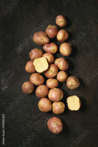 Raw uncooked organic potatoes named miss blush, whole and slice over dark texture background. Top view, copy space