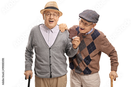 Elderly man sneaking up on another elderly man to grab a bite of his chocolate