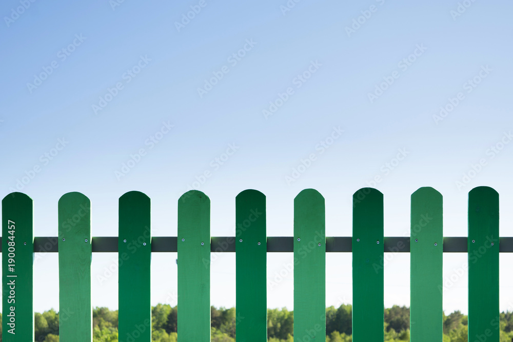 Green wooden fence with grass and blue sky
