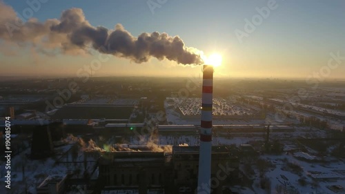 A bird`s eye view of a sky- high chimney with a slow stream of smoke at a wonderful sunset in winter. The cityscape is picturesque photo