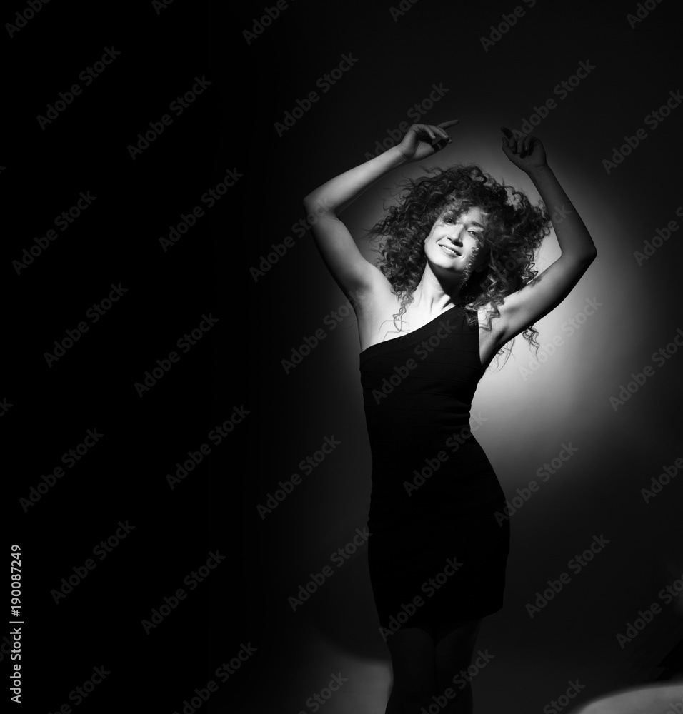 beautiful young girl with curly hair, with a beautiful slender figure in a black dress having fun and dancing at a party, a dark background