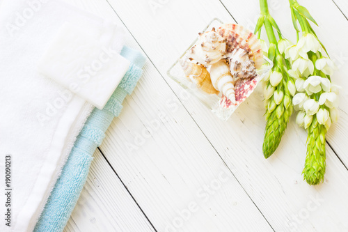 Natural Sea Spa Elements on white wooden background. A glass bowl with sea shells, blue and white towels, hand made soap and fresh white flowers on a white wooden background, top view, flat lay