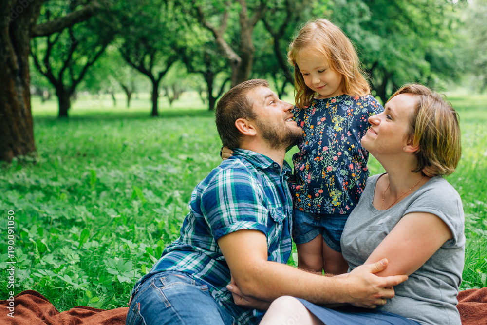 Young happy family of three lying on blanket in the park having fun. Happy parenting concept. Little girl with mother and father outdoors