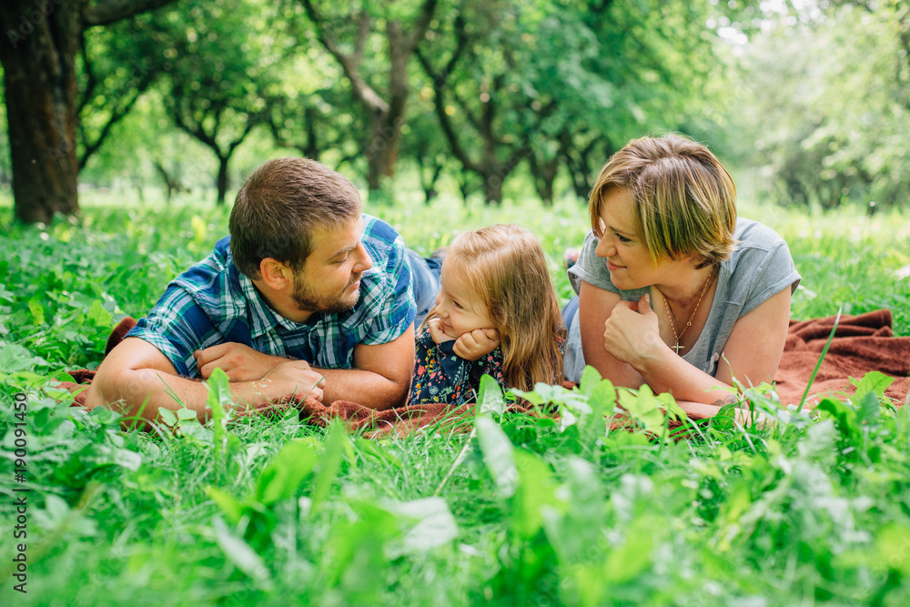 Young happy family of three lying on blanket in the park having fun. Happy parenting concept. Little girl with mother and father outdoors Young happy family of three lying on blanket in the park having fun. Happy parenting concept. Little girl with mother and father outdoors