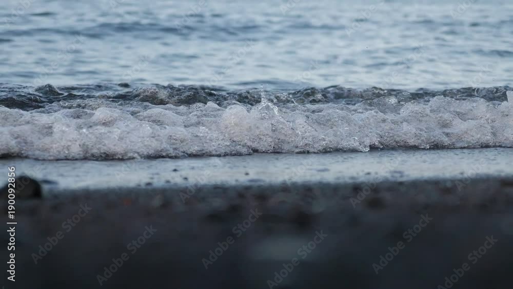 Waves roll on a sandy beach with black volcanic sand. Sandy beach of the sea. Travel concept. Waves roll on a sandy beach with black volcanic sand. Sandy beach of the sea. Travel concept.