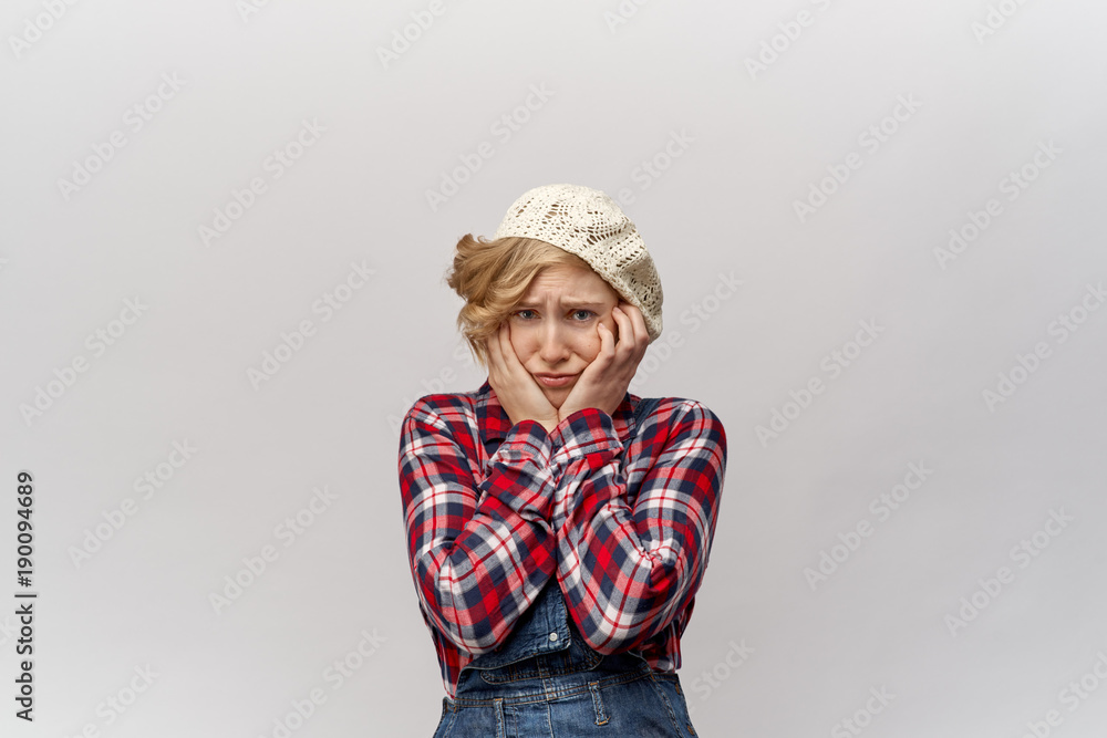 attractive young blond student girl in unfashionable clothes in retro style like a hillbilly in confusion grips her face in hands with disturbed shocked expression. Close-up portrait white background attractive young blond student girl in unfashionable clothes in retro style like a hillbilly in confusion grips her face in hands with disturbed shocked expression. Close-up portrait white background