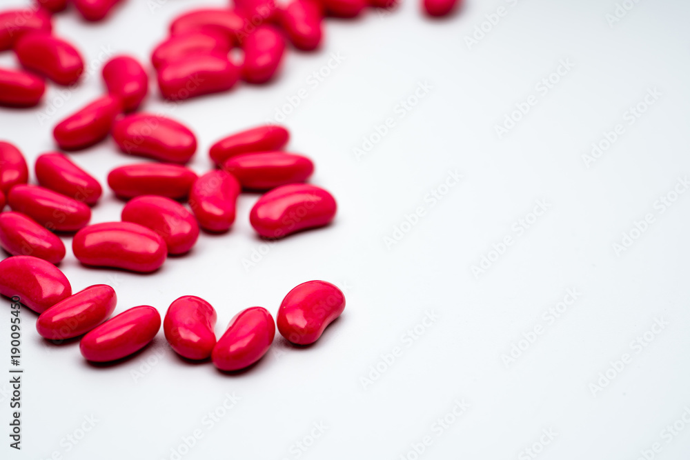 Selective focus of red kidney shape sugar coated tablet pills on white background with copy space Selective focus of red kidney shape sugar coated tablet pills on white background with copy space