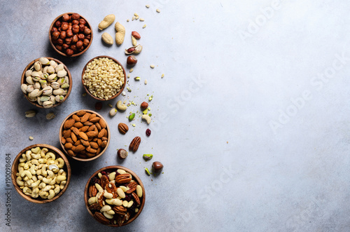 Assortment of nuts in wooden bowls. Cashew, hazelnuts, walnuts, pistachio, pecans, pine nuts, peanut, raisins. Food mix background, top view, copy space, banner.
