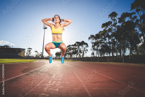 Female fitness model and track athlete sprinting on an athletics track made from tartan © Dewald