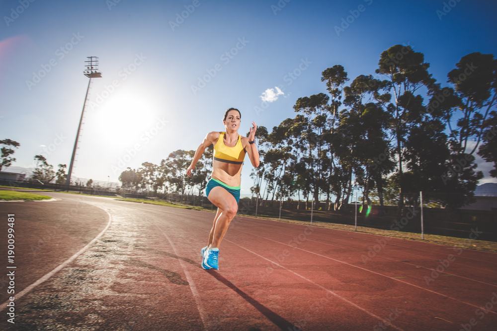 Female fitness model and track athlete sprinting on an athletics track made from tartan