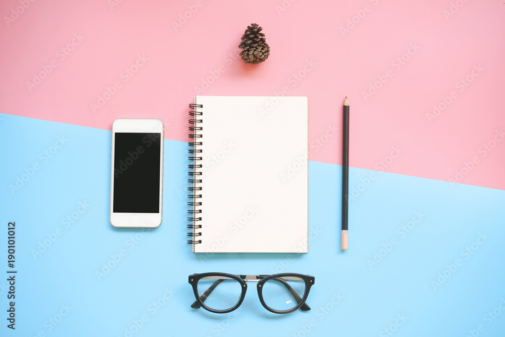 Top view of blank notebook, pencil, smartphone glasses and pine cone on pink and blue background with copy space. Top view of blank notebook, pencil, smartphone glasses and pine cone on pink and blue background with copy space.