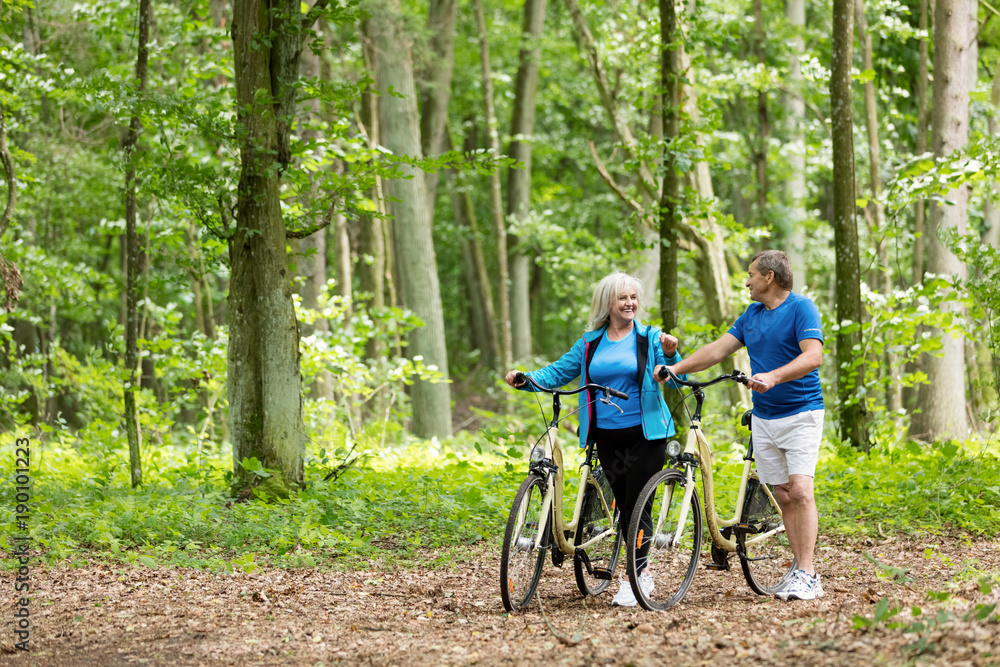 Older marriage standing with bicycles in the forest.