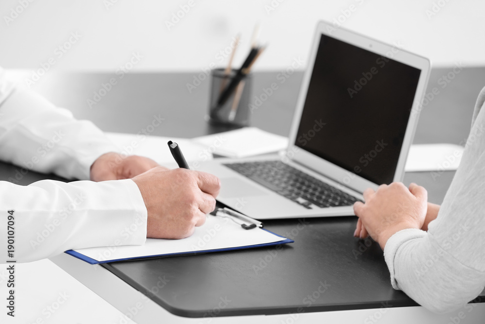 Male doctor filling up application form while consulting patient in clinic, closeup Male doctor filling up application form while consulting patient in clinic, closeup