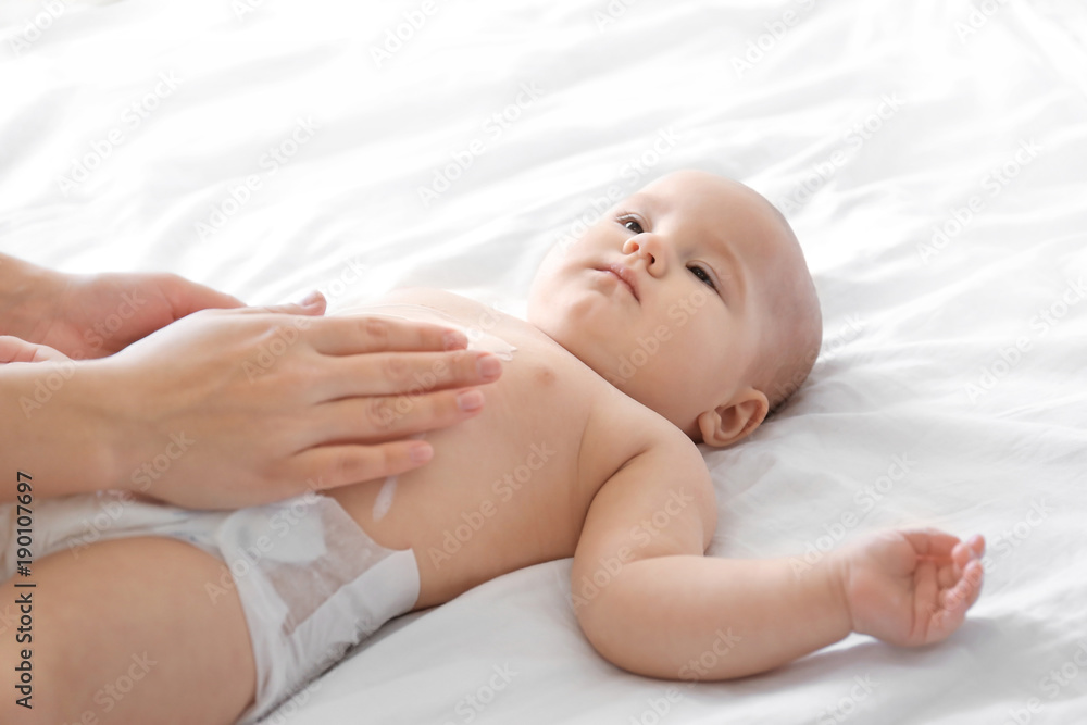 Woman applying body cream on her baby indoors Woman applying body cream on her baby indoors