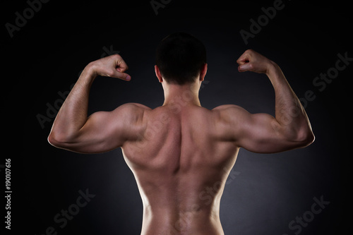Handsome bodybuilder posing on black background, perfect muscular male back