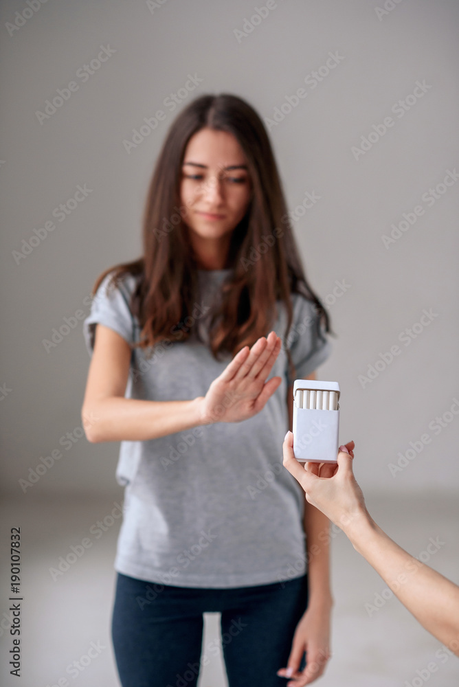 No smoking. Healthy young beautiful girl refusing to take cigarette from package. Portrait of female showing stop sign with hand to cigarettes. Quit smoking, health care concept. No smoking. Healthy young beautiful girl refusing to take cigarette from package. Portrait of female showing stop sign with hand to cigarettes. Quit smoking, health care concept.