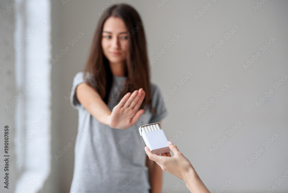No smoking. Healthy young beautiful girl refusing to take cigarette from package. Portrait of female showing stop sign with hand to cigarettes. Quit smoking, health care concept. No smoking. Healthy young beautiful girl refusing to take cigarette from package. Portrait of female showing stop sign with hand to cigarettes. Quit smoking, health care concept.
