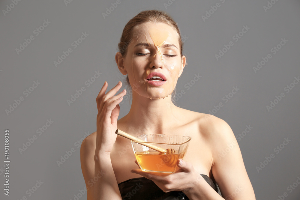 Young woman with honey on her face against grey background. Skin treatment Young woman with honey on her face against grey background. Skin treatment