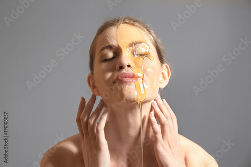 Canvas Print Young woman with honey on her face against grey background