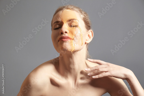 Young woman with honey on her face against grey background. Skin treatment photo