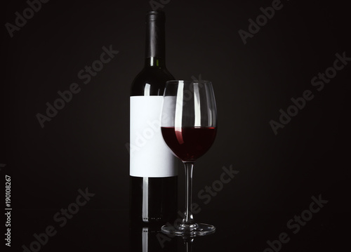 Glass of red wine and bottle with blank label on black background. Mock up for design