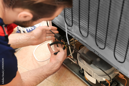 Male technician repairing refrigerator indoors