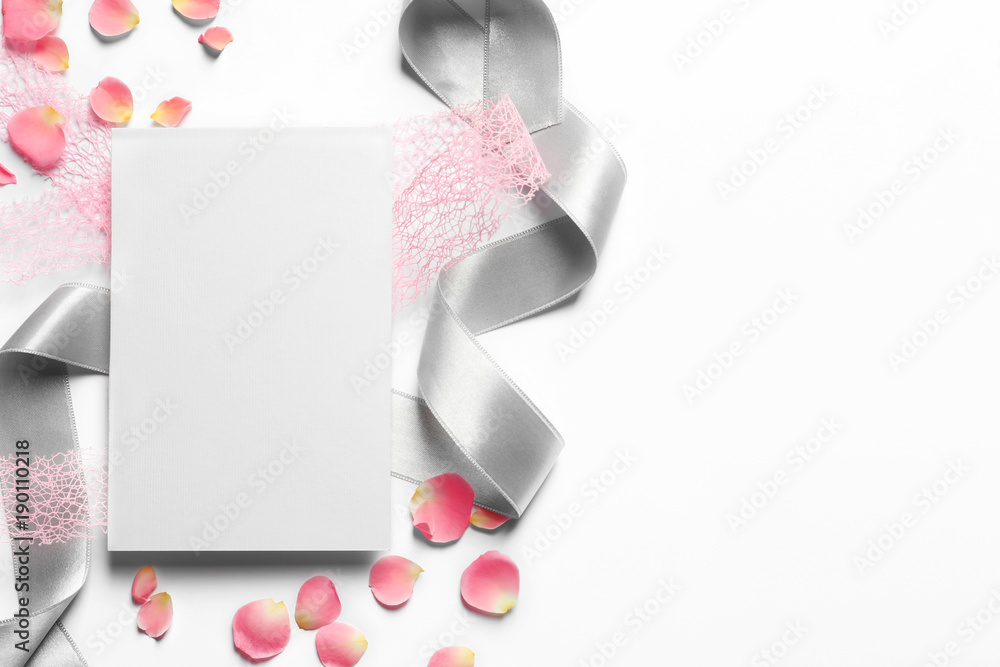 Rose petals, ribbons and empty card on light background