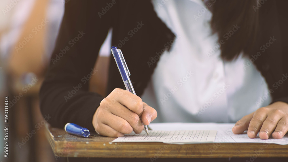 Close up to hand of student holding pen and taking exam in classroom with stress for education test. Close up to hand of student holding pen and taking exam in classroom with stress for education test.