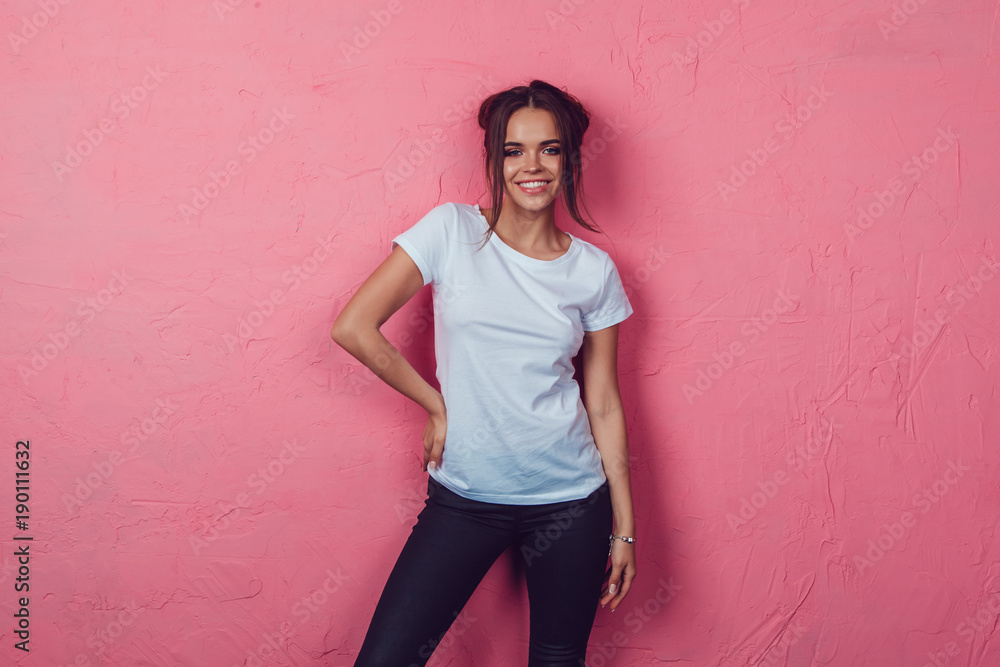 Attractive woman in a white t-shirt stands on a pink background. Mock-up.