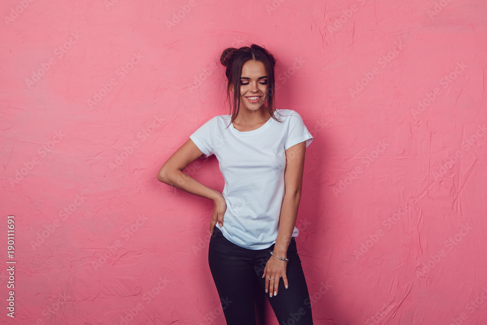 Attractive woman in a white t-shirt stands on a pink background. Mock-up. - obrazy, fototapety, plakaty 