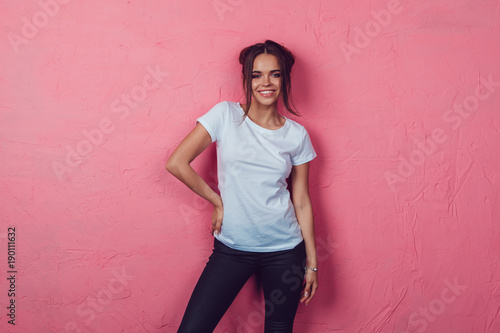 Attractive woman in a white t-shirt stands on a pink background. Mock-up.