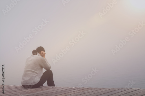 Anonyme traurige Frau sitzt am See im Nebel