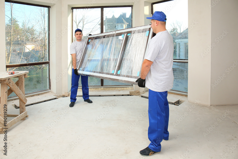 Construction workers carrying window glass indoors