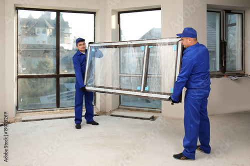 Quadro em tela Construction workers carrying window glass indoors