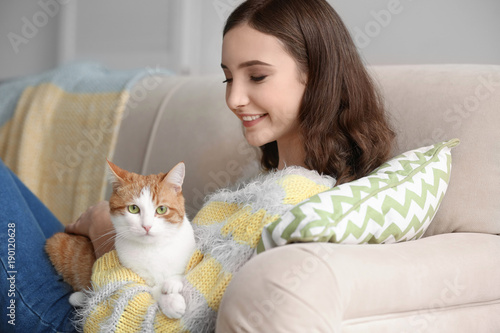 Beautiful young woman with cute cat on sofa at home
