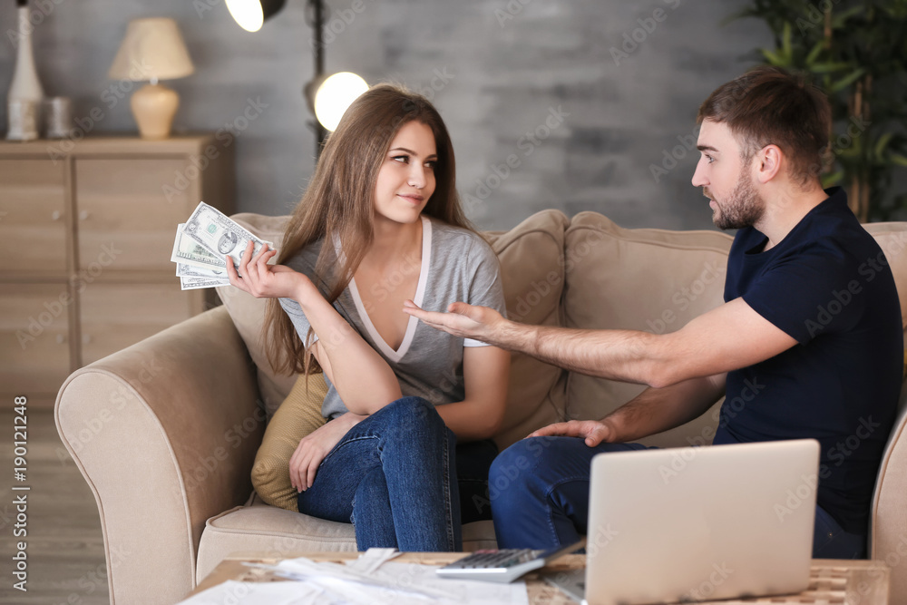 Happy woman with money and indignant man on sofa at home. Problems in relationship