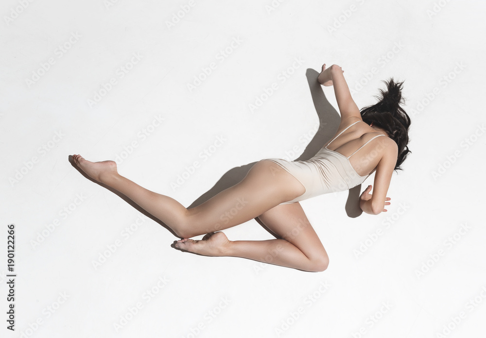Young beautiful dancer in beige dress dancing on gray background Young beautiful dancer in beige dress dancing on gray background