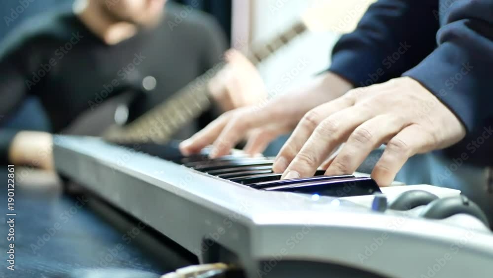 Rock band practice play piano. Musician hands playing on electric piano with guitar player. Music band concert. Man lead guitarist playing electrical guitar on background Rock band practice play piano. Musician hands playing on electric piano with guitar player. Music band concert. Man lead guitarist playing electrical guitar on background