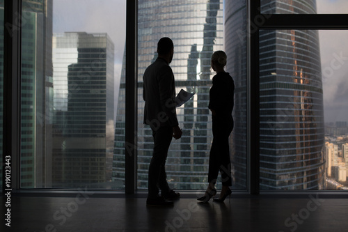 Business people talking negotiating standing near large panoramic window with big city buildings.