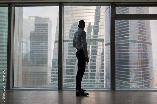 Businessman standing near large panoramic window with big city buildings. © kanashkin