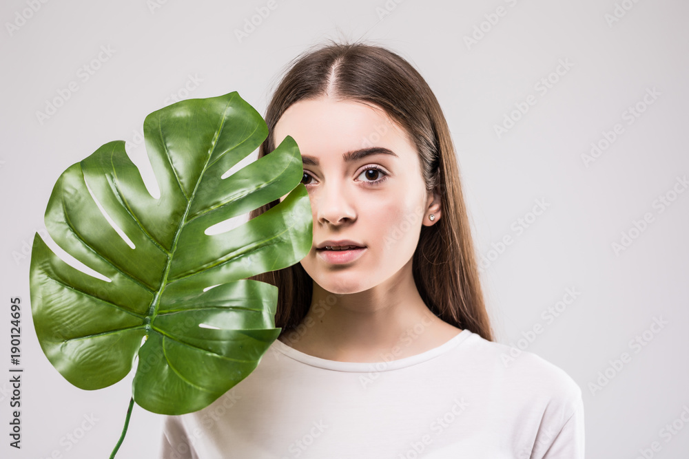 Beauty portrait of an woman with short brunette hair posing with green leaf isolated over gray background. Beauty portrait of an woman with short brunette hair posing with green leaf isolated over gray background.