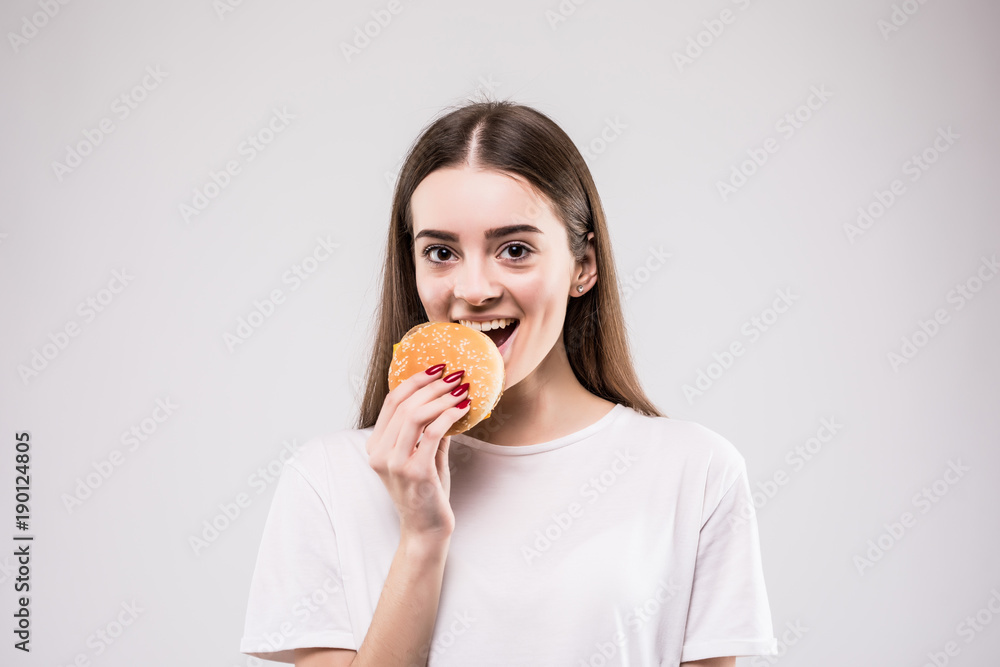 Woman biting burger isolated portrait on gray background. health concept. Woman biting burger isolated portrait on gray background. health concept.