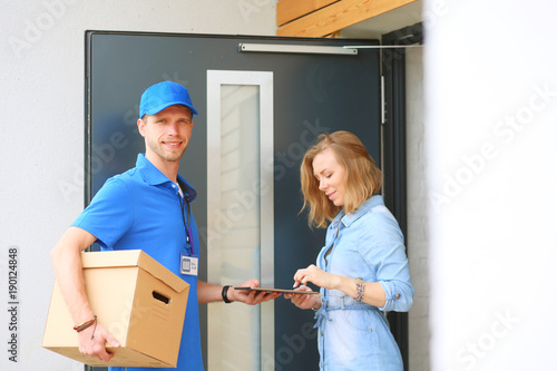 Smiling delivery man in blue uniform delivering parcel box to recipient - courier service concept. Smiling delivery man in blue uniform