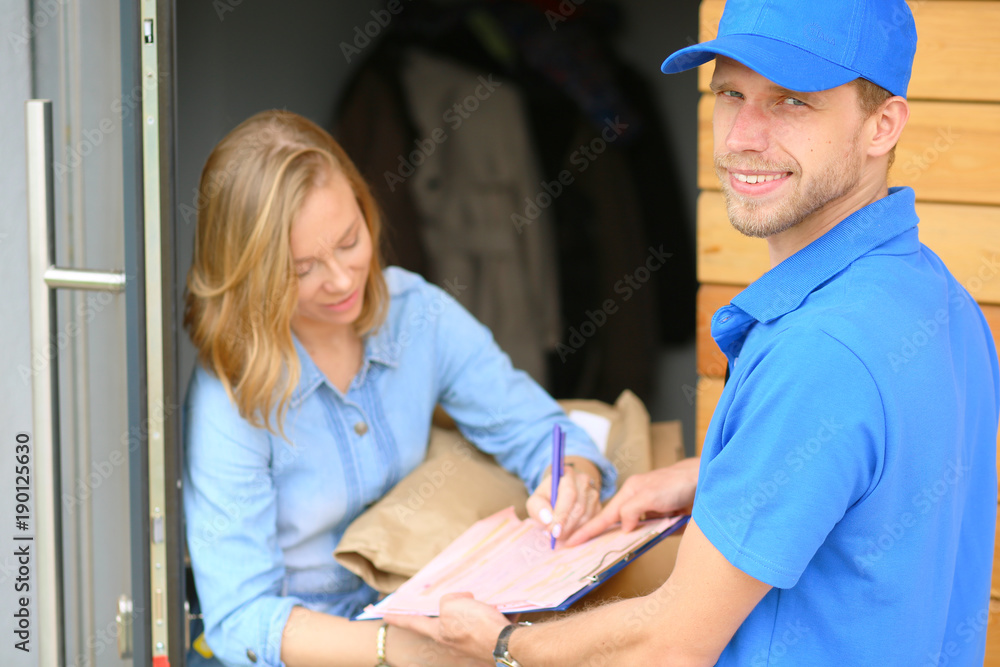 Smiling delivery man in blue uniform delivering parcel box to recipient - courier service concept. Smiling delivery man in blue uniform Smiling delivery man in blue uniform delivering parcel box to recipient - courier service concept. Smiling delivery man in blue uniform