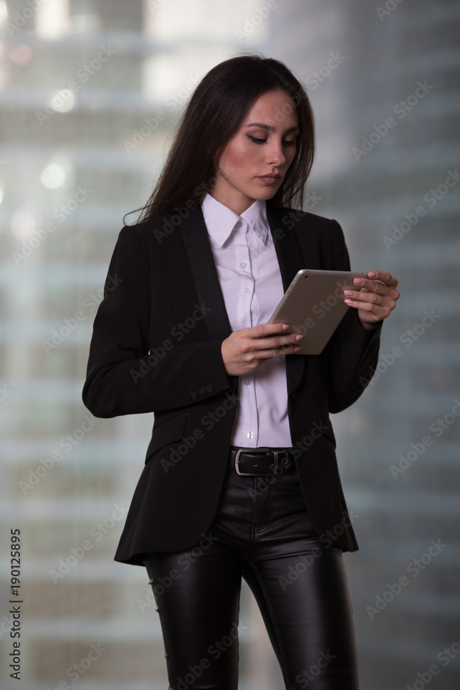 Beautiful business woman with tablet in hands stands near window in office. Beautiful business woman with tablet in hands stands near window in office.
