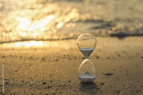 Hourglass close up in a warm golden morning sunlight on a sandy beach starting time for a new day or running of time with side copy space.