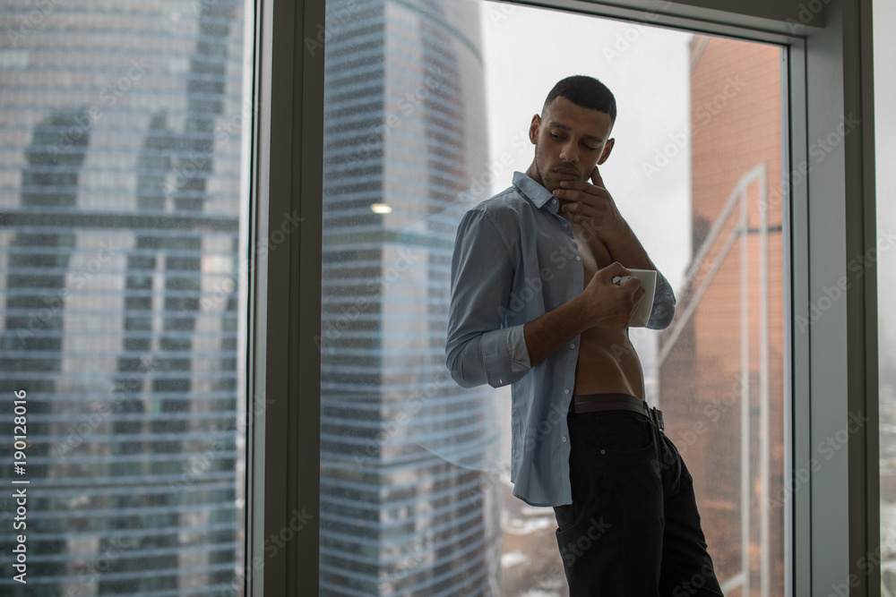 A businessman drinks a morning coffee before the work. Panoramic windows background. A businessman drinks a morning coffee before the work. Panoramic windows background.