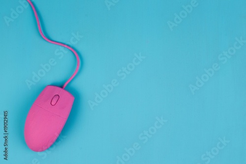 Pink computer mouse on blue background, copy space